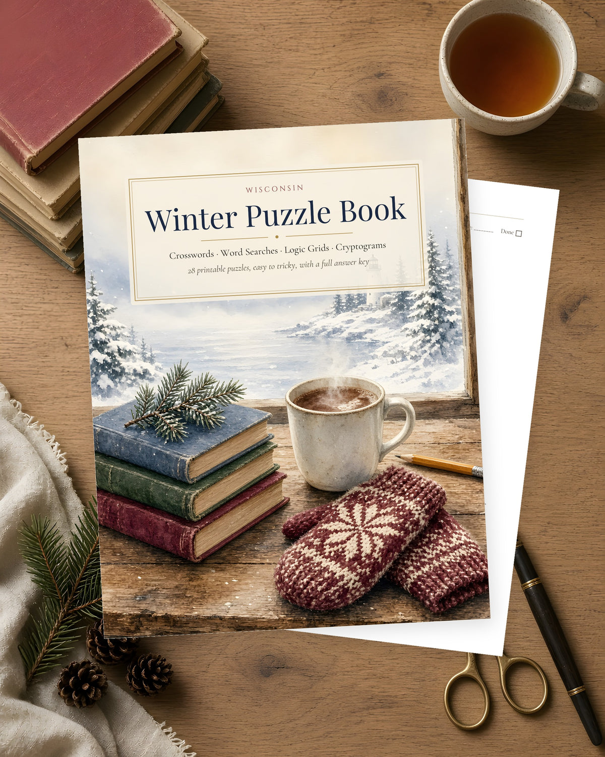 Wisconsin Winter Puzzle Book printable cover on a wooden table with a stack of books, a mug of cocoa, knit mittens and a pencil, showing a snowy pine and lake watercolor scene.